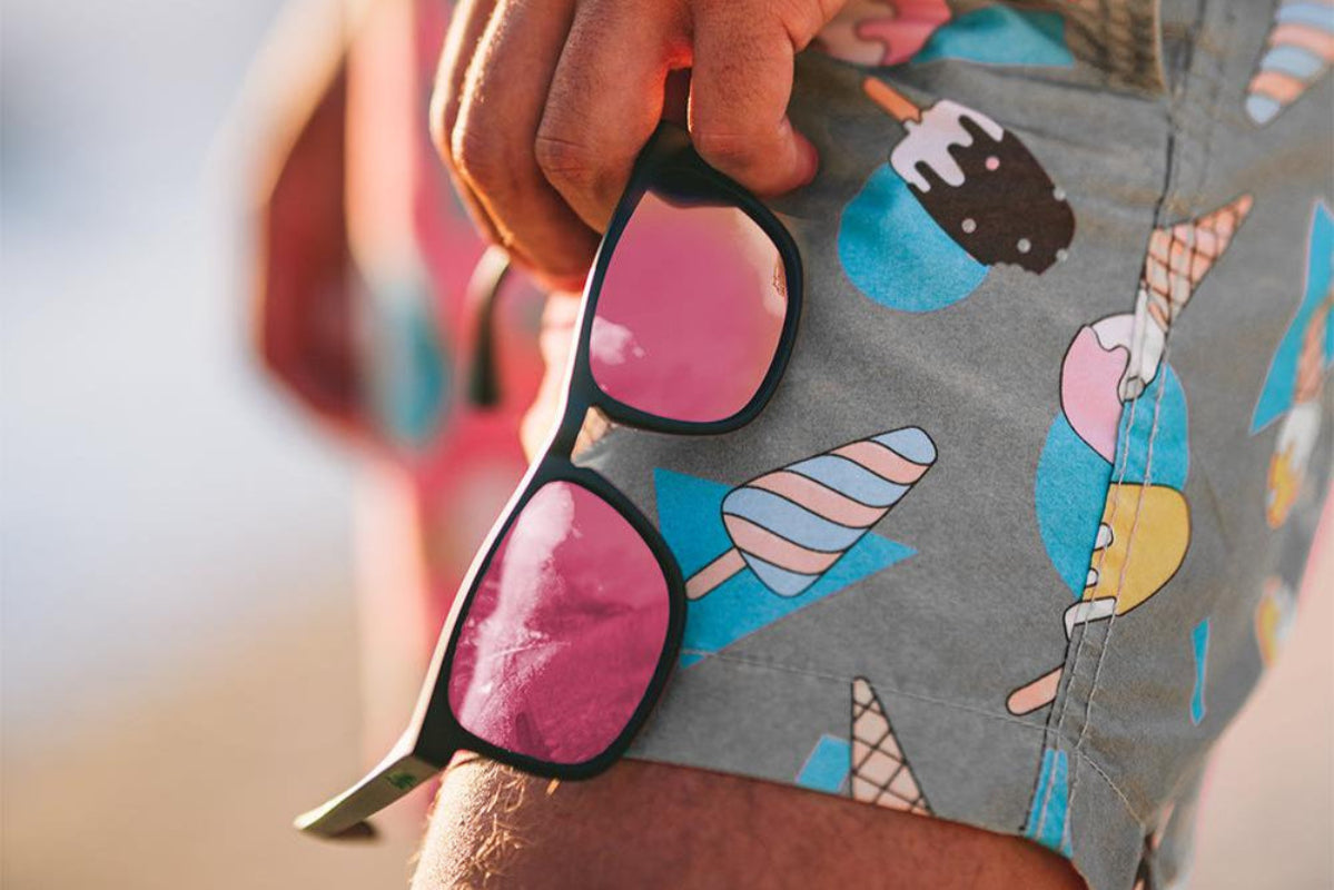 Man wearing mirrored goggles and gray beanie, holding skis in a snowy setting.