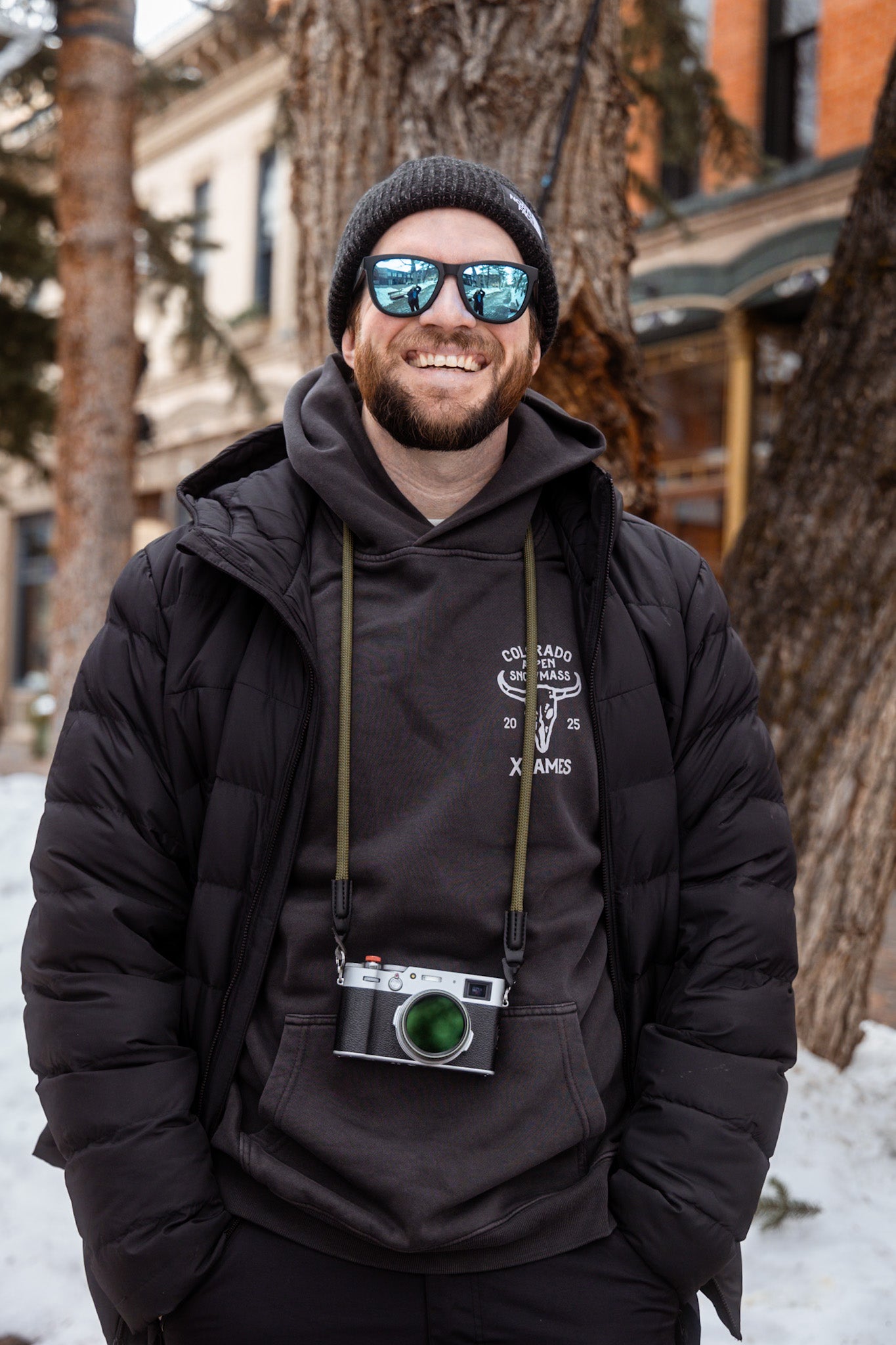 Man wearing mirrored goggles and gray beanie, holding skis in a snowy setting.