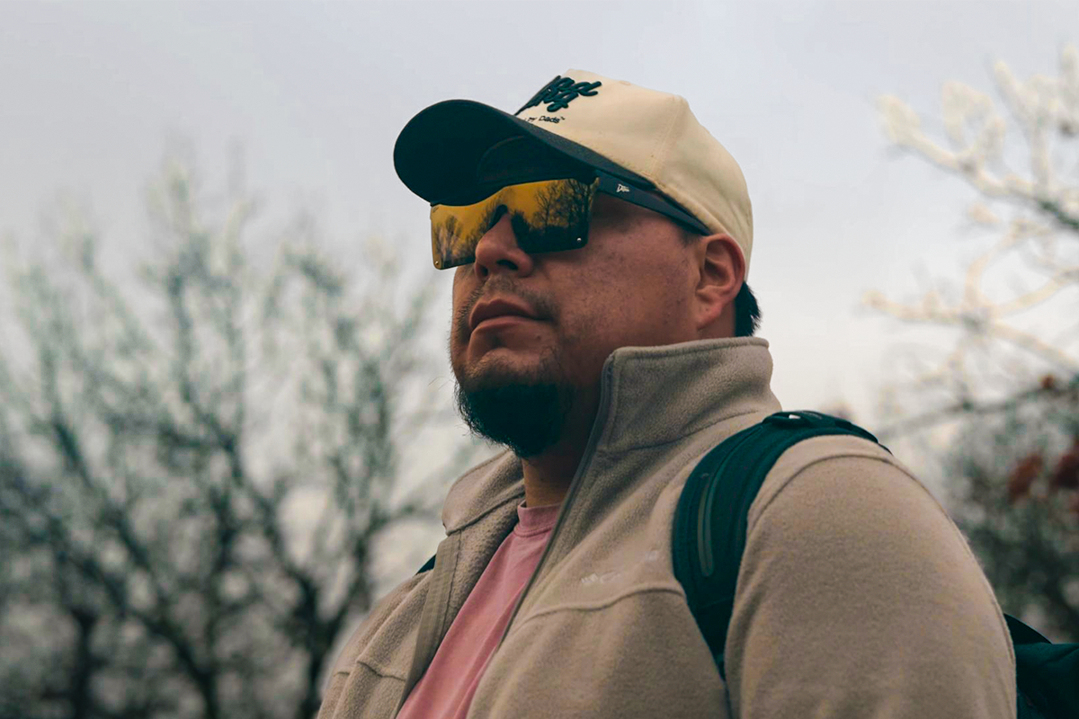 Man wearing mirrored goggles and gray beanie, holding skis in a snowy setting.