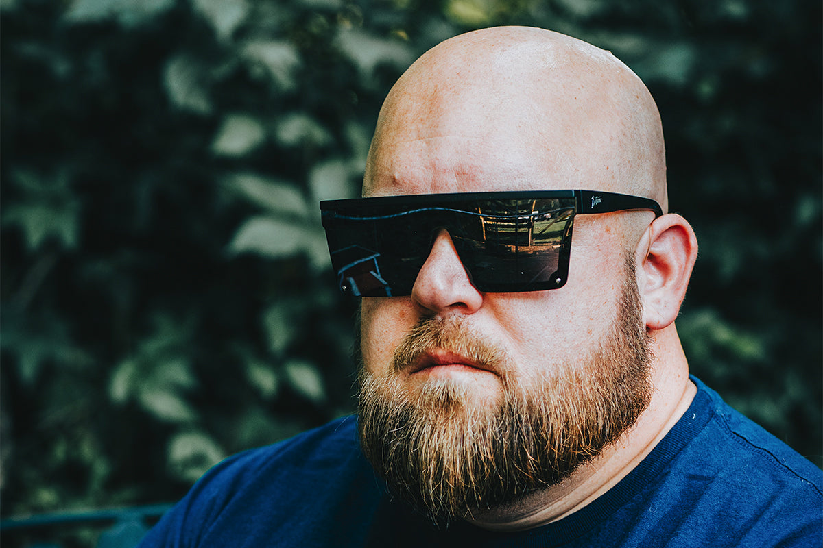 Man wearing mirrored goggles and gray beanie, holding skis in a snowy setting.