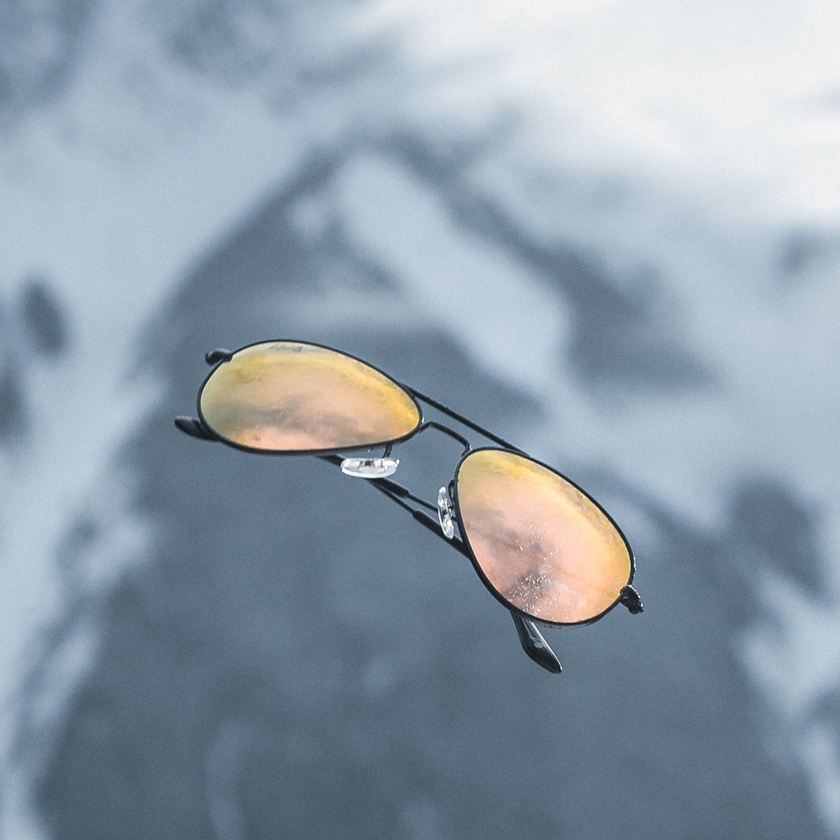 Man wearing mirrored goggles and gray beanie, holding skis in a snowy setting.